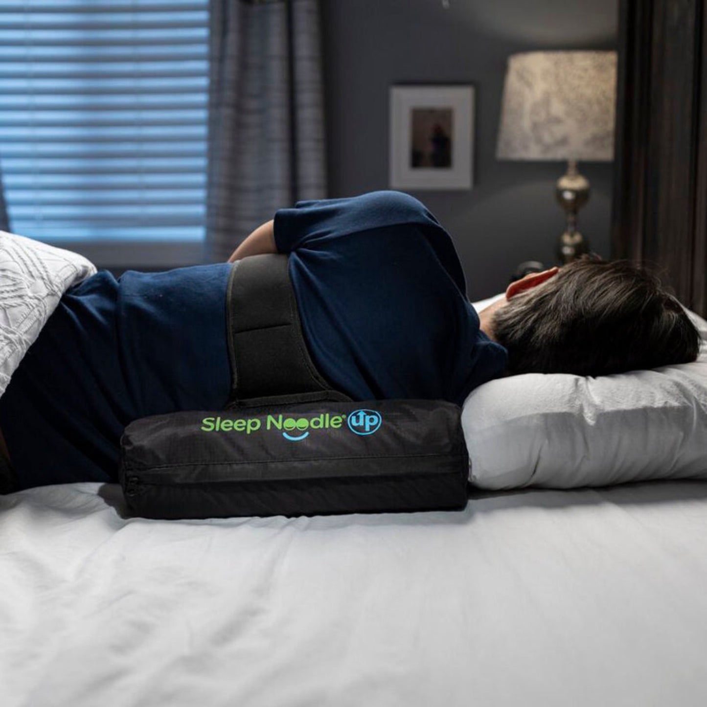 Person lying on a bed with a Sleep Needle Up product, in a bedroom setting.